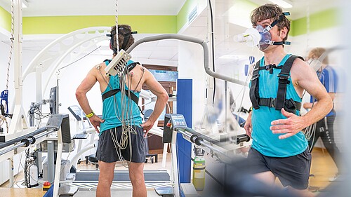 Der gleiche Mann aus zwei Perspektiven: Zuerst steht er auf dem Laufband, verkabelt und mit Sauerstoffmaske für die Leistungsdiagnostik. Dann läuft er auf dem Laufband mit derselben Ausrüstung, während eine Messung während des Laufens durchgeführt wird.